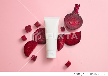 Scene for advertising and branding cosmetic with beetroot ingredient. An empty white plastic tube on pink background with beet slices. Beetroot contains many important nutrients good for beauty 105022665
