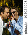 Young happy couple outdoors drinking cold drink from glass bottle with straw. Side view of man and woman drinking soft drink and smiling. 105024998