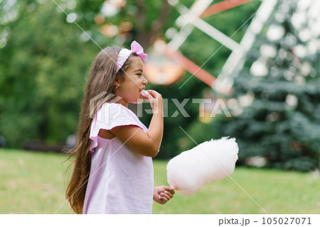 Funny girl in pink dress eats cotton candy in summer in the park Funny girl in pink dress eats cotton candy in summer in the park 105027071