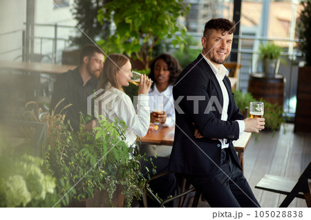 Focus on handsome businessman standing with beer glass and smiling. Blurred people on background. Team meeting 105028838