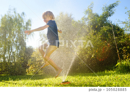 Funny little boy playing with garden sprinkler in sunny backyard. Preschooler child laughing, jumping and having fun with spray of water. Funny little boy playing with garden sprinkler in sunny backyard. Preschooler child laughing, jumping and having fun with spray of water. 105028885