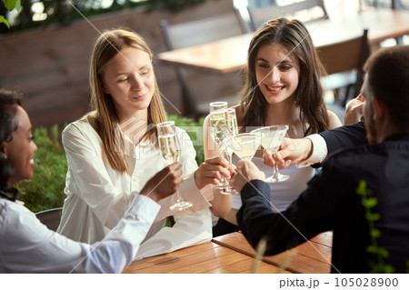 Cheerful young people, colleagues meeting in restaurant after work, celebrating project, drinking champagne and talking Cheerful young people, colleagues meeting in restaurant after work, celebrating project, drinking champagne and talking 105028900
