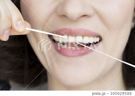 Woman brushing her teeth with dental tape close-up. Small distance between teeth Woman brushing her teeth with dental tape close-up. Small distance between teeth 105029588