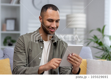 Close-up photo. Young hispanic man using tablet at home. dials, chats, talks via video call. 105029691