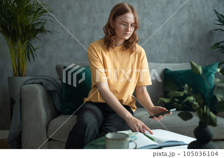 Young gorgeous woman holding 20 euro banknotes filling up bills work with financial papers at home count on calculator before paying taxes receipts online by phone.  105036104