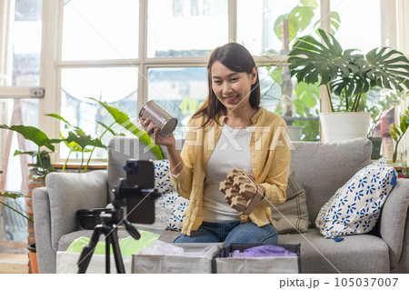 Asian female holding cans and paper boxes live stream talk on smartphone introducing waste 105037007