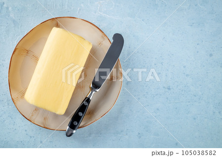 A block of butter with a knife on a plate, overhead flat lay shot A block of butter with a knife on a plate, overhead flat lay shot 105038582