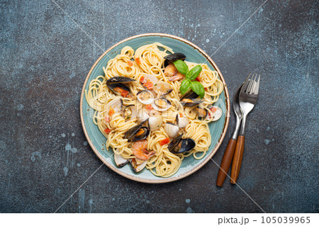 Italian seafood pasta spaghetti with mussels, shrimps, clams in tomato sauce with green basil on plate on rustic blue concrete background top view. Mediterranean cuisine Italian seafood pasta spaghetti with mussels, shrimps, clams in tomato sauce with green basil on plate on rustic blue concrete background top view. Mediterranean cuisine 105039965