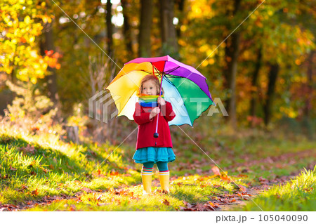 Kid with umbrella playing in autumn rain. 105040090
