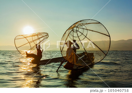 Myanmar travel attraction landmark - two traditional Burmese fishermen at Inle lake, Myanmar famous for their distinctive one legged rowing style on sunrise sunset Myanmar travel attraction landmark - two traditional Burmese fishermen at Inle lake, Myanmar famous for their distinctive one legged rowing style on sunrise sunset 105040758