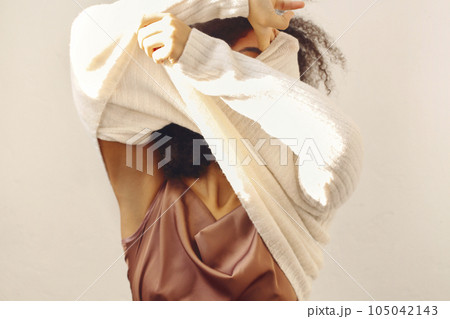 Young african american woman taking off warm and soft white knitted sweater, undressing at home 105042143