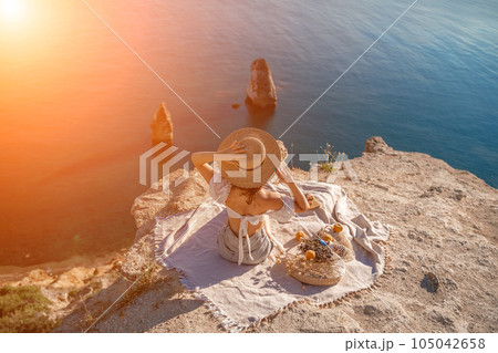 woman sea travel. photo of a beautiful woman with long blond hair in a pink shirt and denim shorts and a hat having a picnic on a hill overlooking the sea 105042658