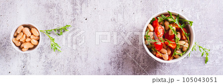 Homemade salad of white beans, cherry tomatoes and arugula in a bowl top view web banner 105043051