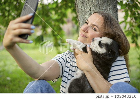 Woman in a t-shirt and jeans with a husky puppy takes a photo or selfie 105043210