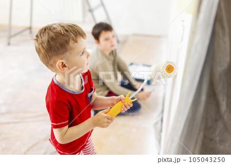 Children paint a wall with brush and roller in white color. Children paint wall 105043250