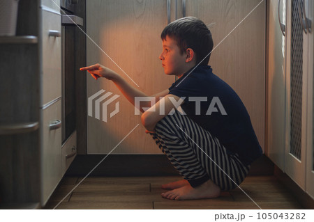 A child is sitting near the oven in the kitchen and waiting. 105043282
