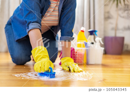 Woman in rubber gloves is using floor brush to cleaning floor 105043345