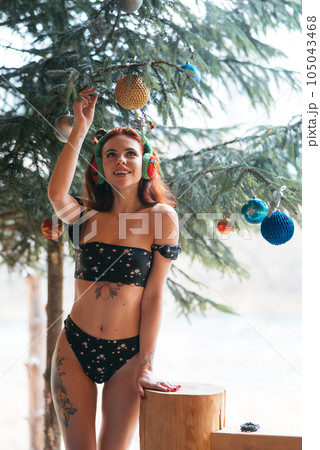 Beautiful girl in bikini with Christmas tree and snow-covered trees in winter Beautiful girl in bikini with Christmas tree and snow-covered trees in winter 105043468