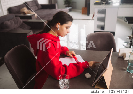 Beautiful girl with headphones is holding a pen in her hand and writing information from tablet to a notebook Beautiful girl with headphones is holding a pen in her hand and writing information from tablet to a notebook 105043585