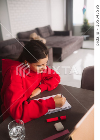 Beautiful girl with headphones is holding a pen in her hand and writing information from tablet to a notebook Beautiful girl with headphones is holding a pen in her hand and writing information from tablet to a notebook 105043595