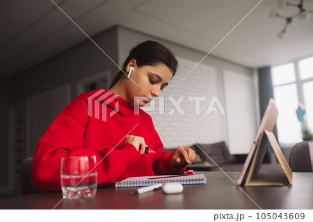 Beautiful girl with headphones is holding a marker and line in her hand and writing information from tablet to a notebook Beautiful girl with headphones is holding a marker and line in her hand and writing information from tablet to a notebook 105043609