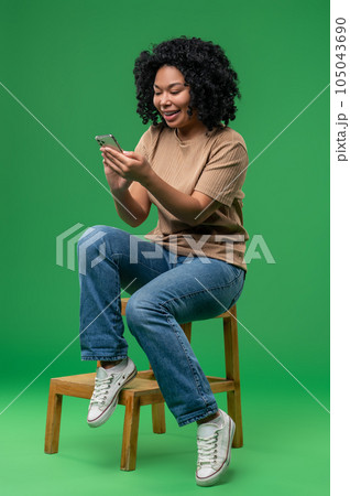 Excited young woman sitting on the chair with a phone in hands 105043690