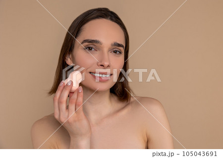 Woman holding soft facial cellulose sponge washing or exfoliating face isolated on beige background. 105043691