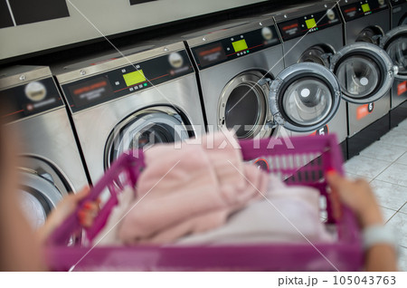 Woman in the public room to wash her cloths, self service commercial laundry and drying machine in a public room. Woman in the public room to wash her cloths, self service commercial laundry and drying machine in a public room. 105043763