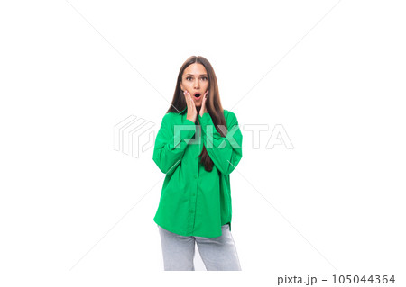 young brown-haired female model with brown eyes in a green shirt is surprised on a white background 105044364