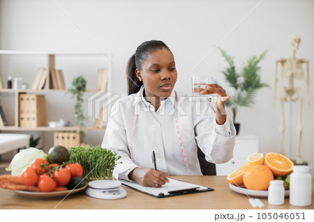 Nutrition specialist checking fluid in glass at workplace Nutrition specialist checking fluid in glass at workplace 105046051