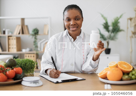 Female with medicine bottle writing on paper in office Female with medicine bottle writing on paper in office 105046056