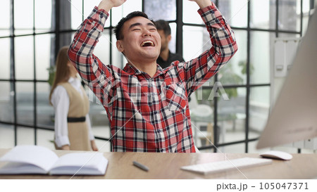 Happy young Asian man sitting in the office at the table Happy young Asian man sitting in the office at the table 105047371