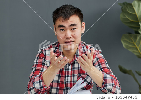 Young Asian man sitting at the table with his chin propped Young Asian man sitting at the table with his chin propped 105047455