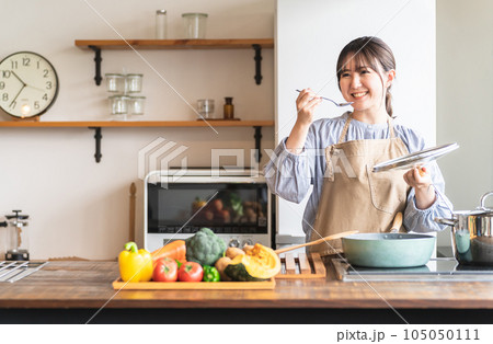 キッチンで料理の味見をするエプロン姿の女性・主婦 105050111