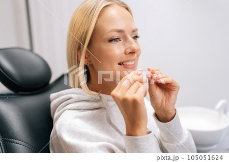 Closeup headshot of pretty young woman patient holding invisible braces aligner during consultation at dentistry clinic. Closeup of mobile orthodontic appliance for dental correction. Closeup headshot of pretty young woman patient holding invisible braces aligner during consultation at dentistry clinic. Closeup of mobile orthodontic appliance for dental correction. 105051624