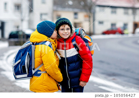 Two little kids boys of elementary class walking to school during snowfall. Happy children having fun and playing with first snow. Siblings and best friends with backpack in colorful winter clothes. Two little kids boys of elementary class walking to school during snowfall. Happy children having fun and playing with first snow. Siblings and best friends with backpack in colorful winter clothes. 105056427
