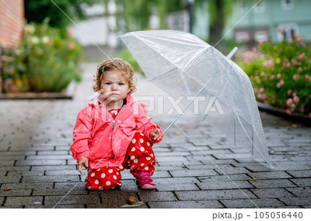 Cute adorable baby girl discovering snail on a walk. Beautiful curly toddler child having fun on rainy day. With big umbrella, child in waterproof clothes Cute adorable baby girl discovering snail on a walk. Beautiful curly toddler child having fun on rainy day. With big umbrella, child in waterproof clothes 105056440