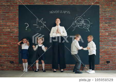 Mindfulness. Young woman in formal wear standing by blackboard with little children. Education, business and psychology lessons 105058529