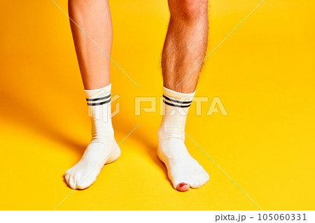 Male and female legs standing in white socks against bright yellow studio background 105060331