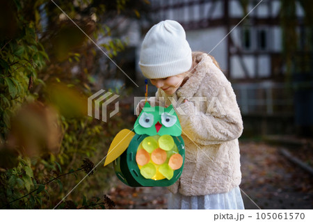 Little preschool kid girl holding selfmade traditional owl lanterns with candle for St. Martin procession. child happy about children and family parade in kindergarten. German tradition Martinsumzug 105061570