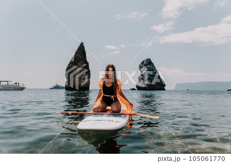 Woman sea sup. Close up portrait of happy young caucasian woman with long hair looking at camera and smiling. Cute woman portrait in bikini posing on sup board in the sea Woman sea sup. Close up portrait of happy young caucasian woman with long hair looking at camera and smiling. Cute woman portrait in bikini posing on sup board in the sea 105061770