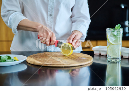Closeup of a woman's hands preparing cold cocktail with lemon, mint leaves and ice 105062930