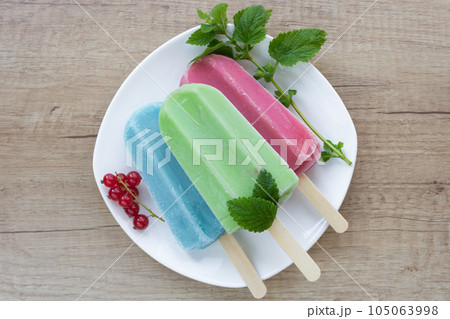 Blue, green and pink ice cream on a white plate with a mint leaf and a sprig of red berries. Blue, green and pink ice cream on a white plate with a mint leaf and a sprig of red berries. 105063998