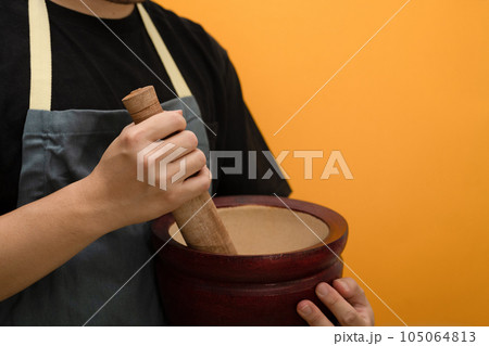Man wearing apron holding mortar and pestle isolated on yellow background with empty space 105064813