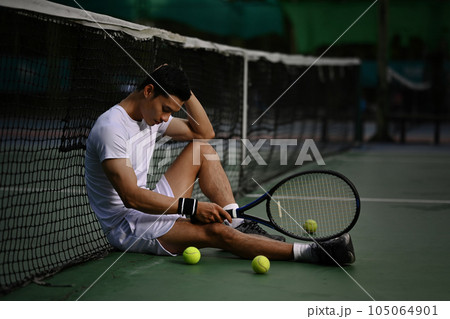 Disappointed asian male tennis player sitting on the court, upset about competition loss, failure emotions Disappointed asian male tennis player sitting on the court, upset about competition loss, failure emotions 105064901