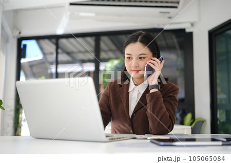 Young entrepreneur having cell phone conversation with client and using laptop on white office desk 105065084