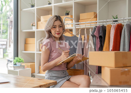 Asian woman entrepreneur of online sell clothing using laptop and taking note in notebook on desk in home office Asian woman entrepreneur of online sell clothing using laptop and taking note in notebook on desk in home office 105065455