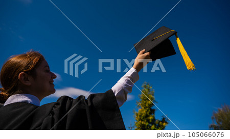 A woman throws her graduation cap against the blue sky. 105066076