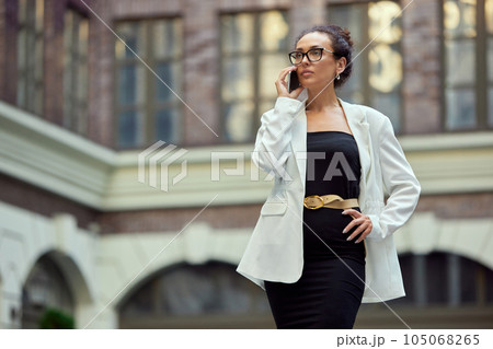 Serious, concentrated, confident business woman walking outside the office and talking on mobile phone Serious, concentrated, confident business woman walking outside the office and talking on mobile phone 105068265