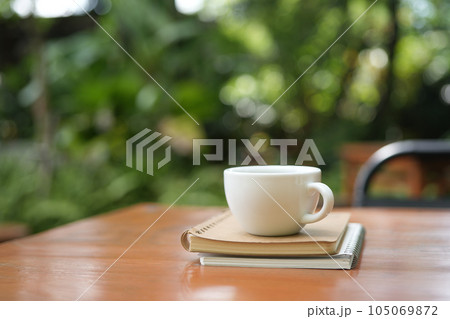 White coffee cup and bronze spoon on brown wooden table with green lush background 105069872